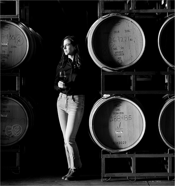 Nicole Hitchcock, head winemaker at J Vineyards and Winery, looking to the side next to barrels of wine.