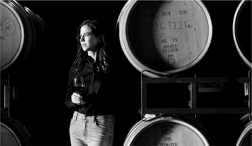 Nicole Hitchcock, head winemaker at J Vineyards and Winery, looking to the side next to barrels of wine.