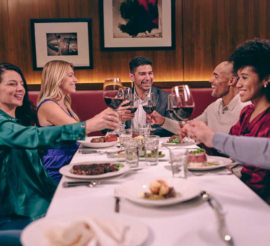 Two hands clinking glasses of red wine in a celebratory toast while enjoying dinner at The Capital Grille.