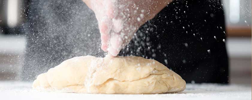 The Capital Grille's pastry chef dusting flour over a ball of dough on a floured surface, preparing for baking.
