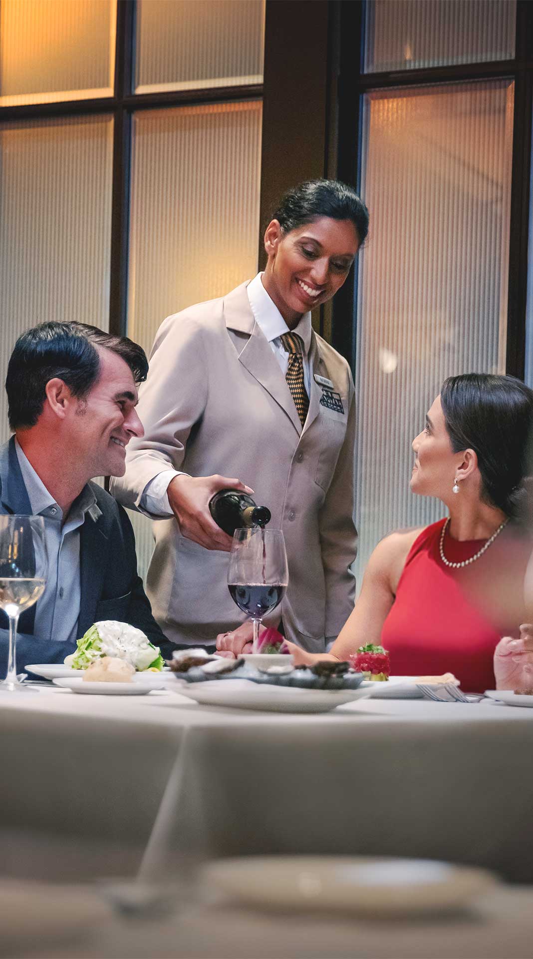 Server pouring wine for a couple at a romantic table setting.